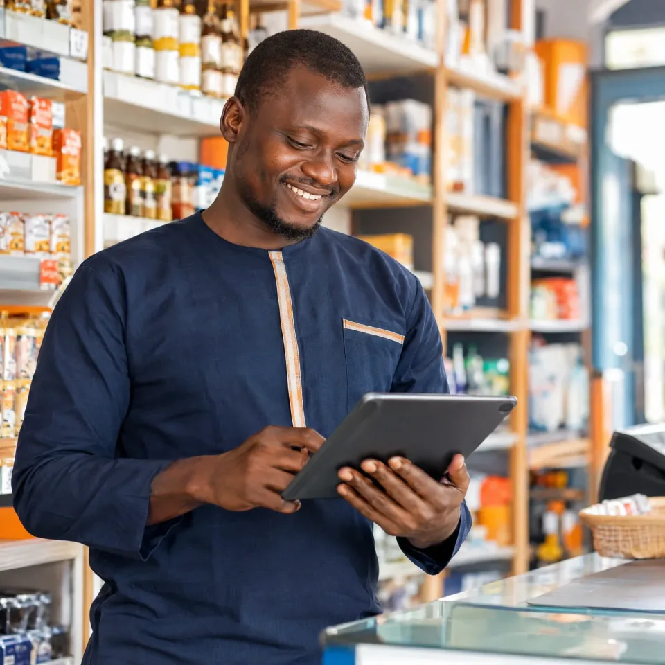 Un commerçant souriant consulte une tablette dans sa boutique